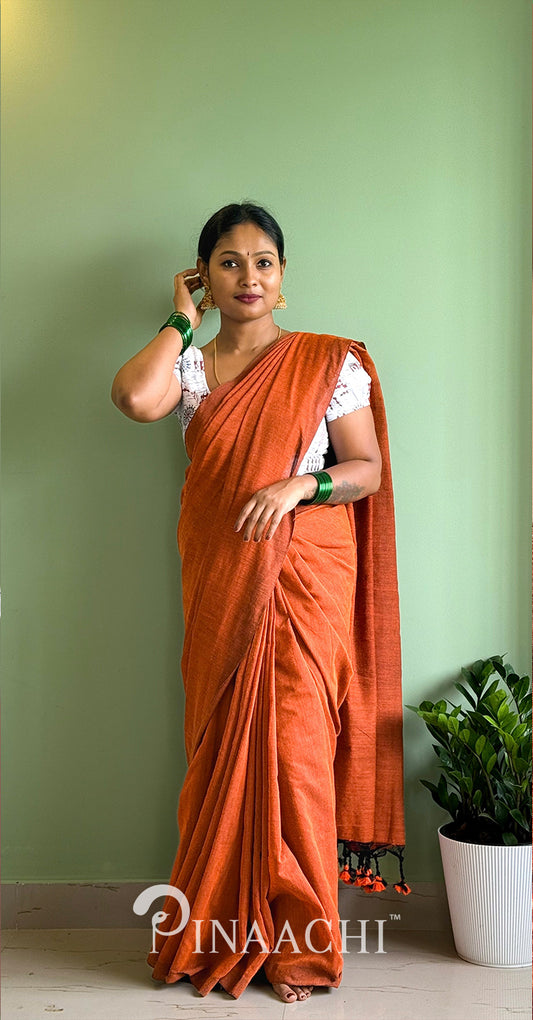 Elegant woman modeling a handspun rust orange cotton saree against a green backdrop