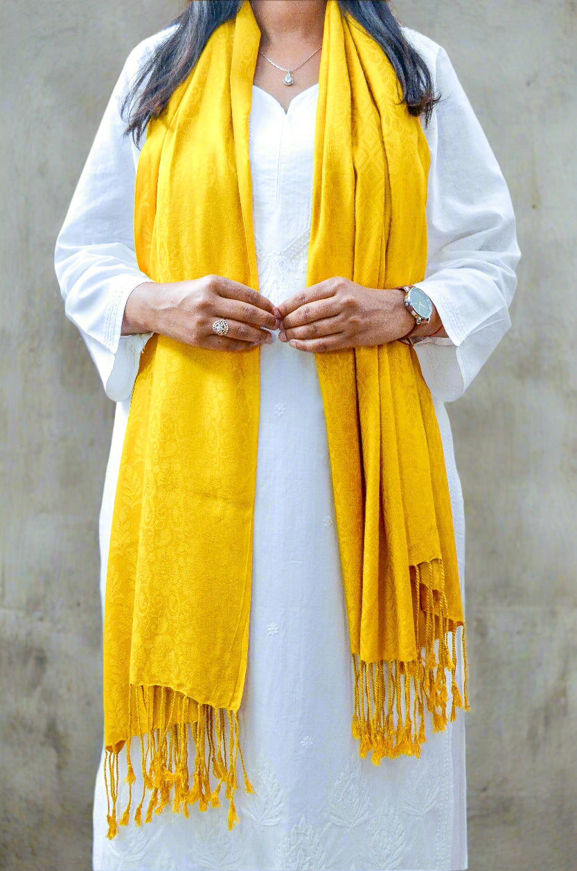 Elegant mustard yellow jacquard stole draped over a white outfit with fringed edges