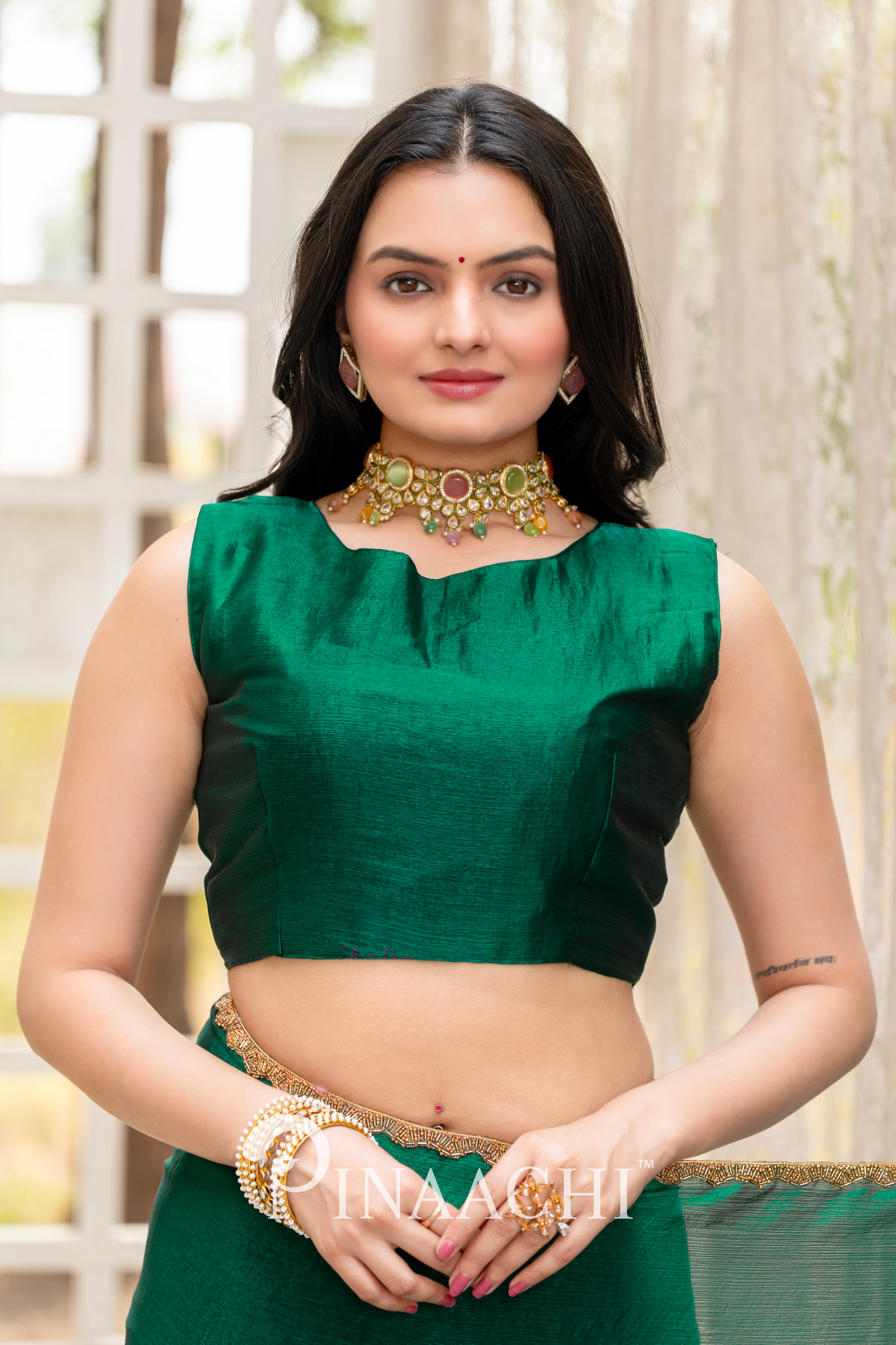 Woman wearing Pinaachi bottle green chiffon saree blouse with gold jewelry in indoor setting