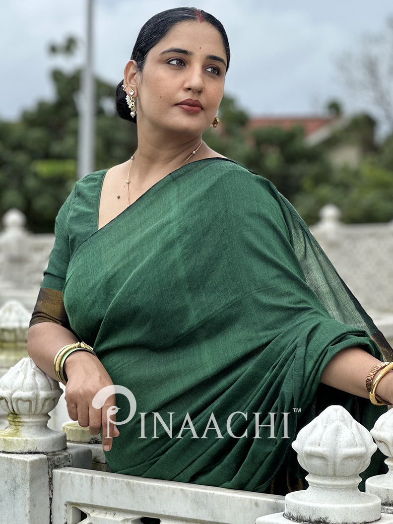 Elegant woman wearing an emerald green cotton saree, showcasing a classic drape and stunning backdrop