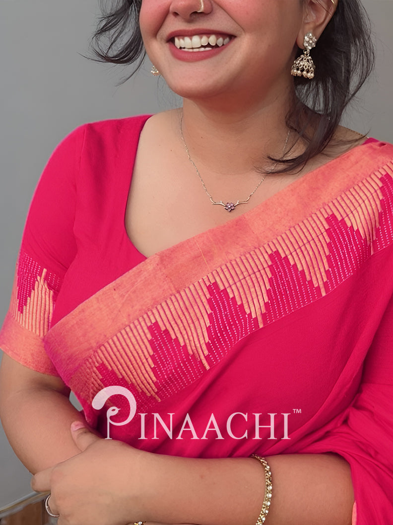 Woman wearing a pink saree with intricate patterns, smiling against a gray background. Pinaachi brand visible.