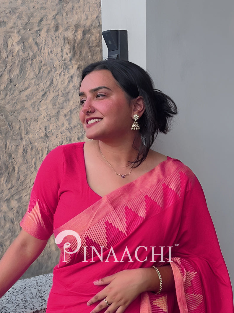 Woman wearing a pink saree with a visible brand logo against a neutral background