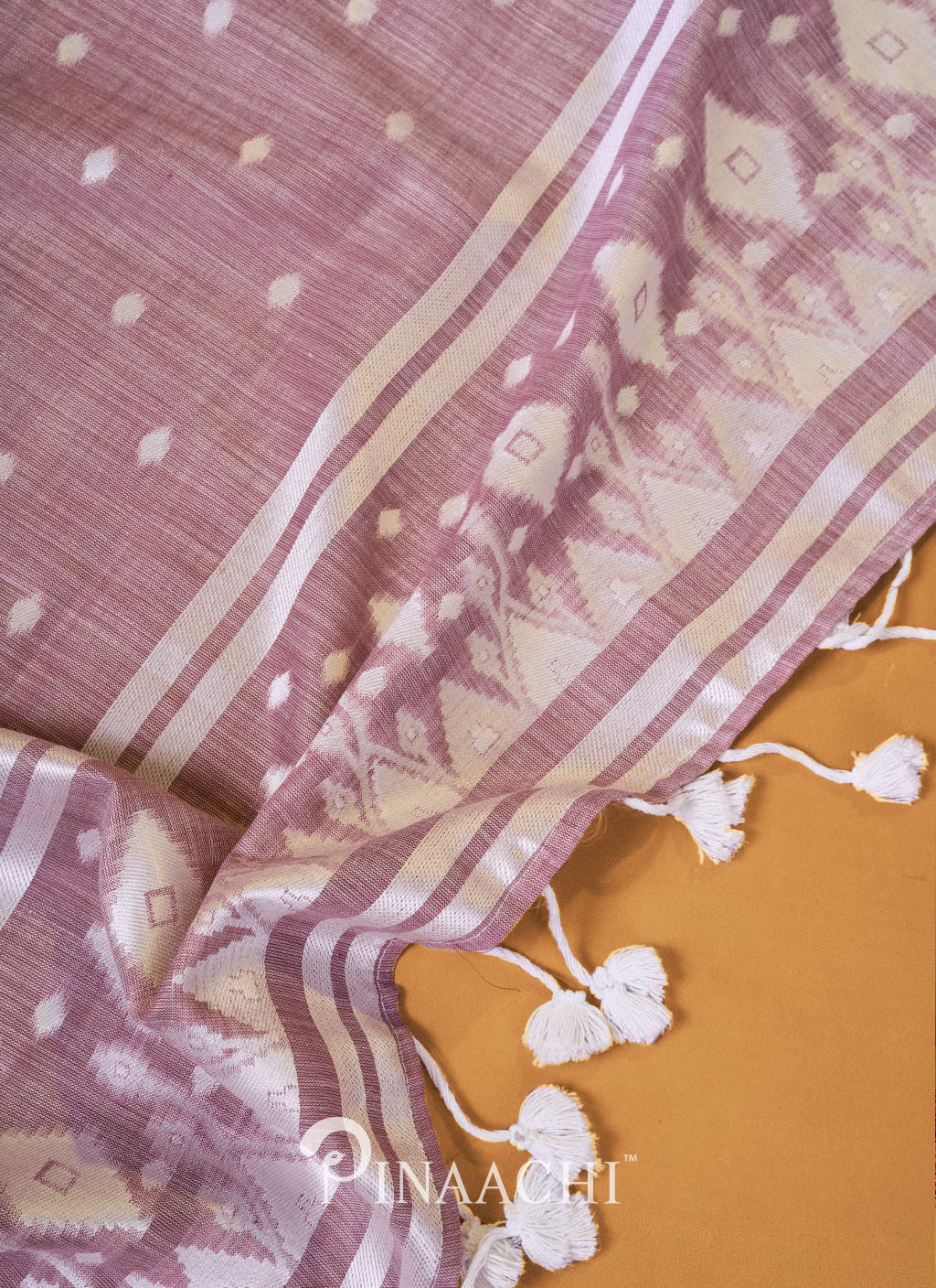 Light purple pinaachi jamdani saree with white geometric patterns and tassels on beige background