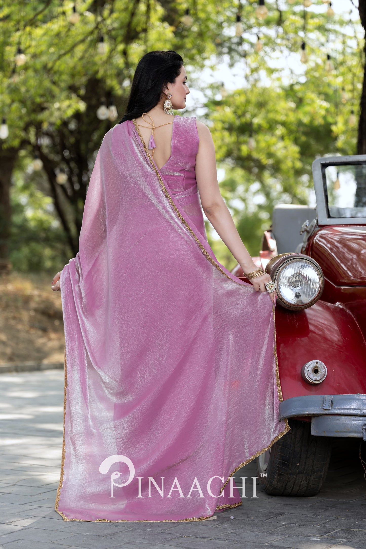 Woman wearing Pinaachi lavender chiffon saree with gold border standing beside vintage red car outdoors