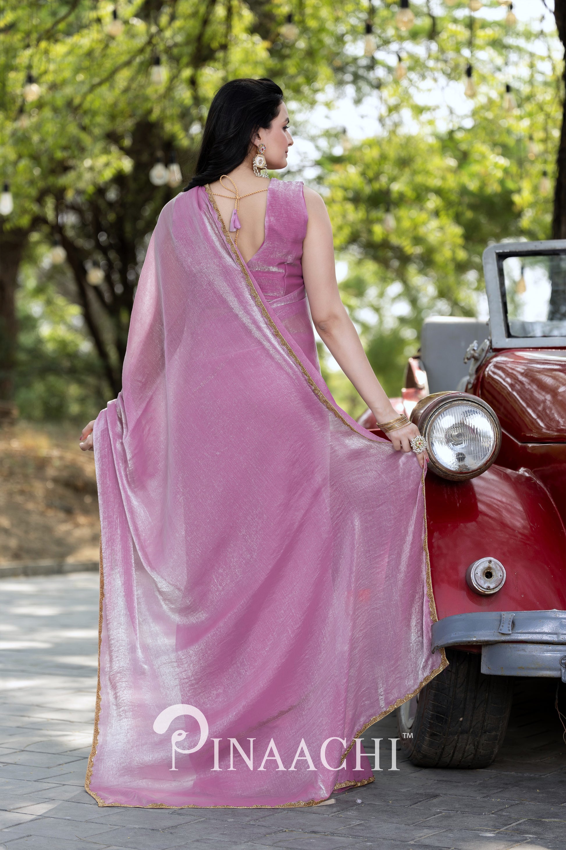Woman wearing Pinaachi lavender chiffon saree with gold border standing beside vintage red car outdoors