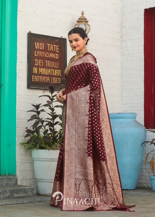 Woman wearing Pinaachi Maroon Banarasi Silk Saree with intricate gold patterns and traditional design