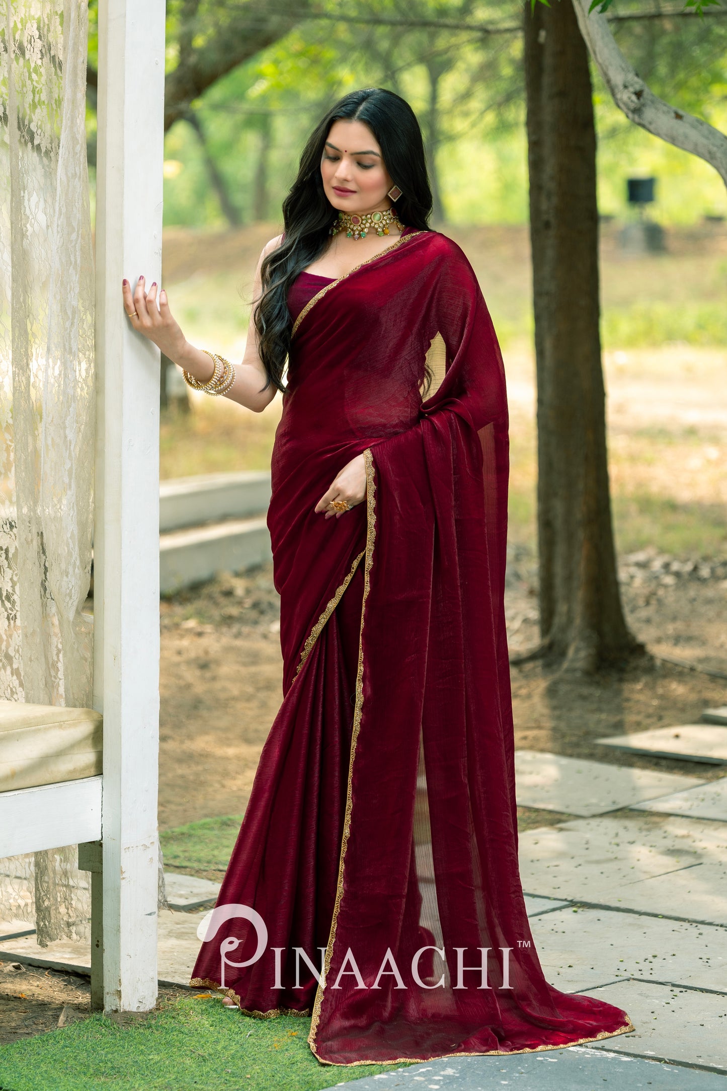 Elegant Pinaachi maroon chiffon saree worn by woman with gold border detail and matching jewelry