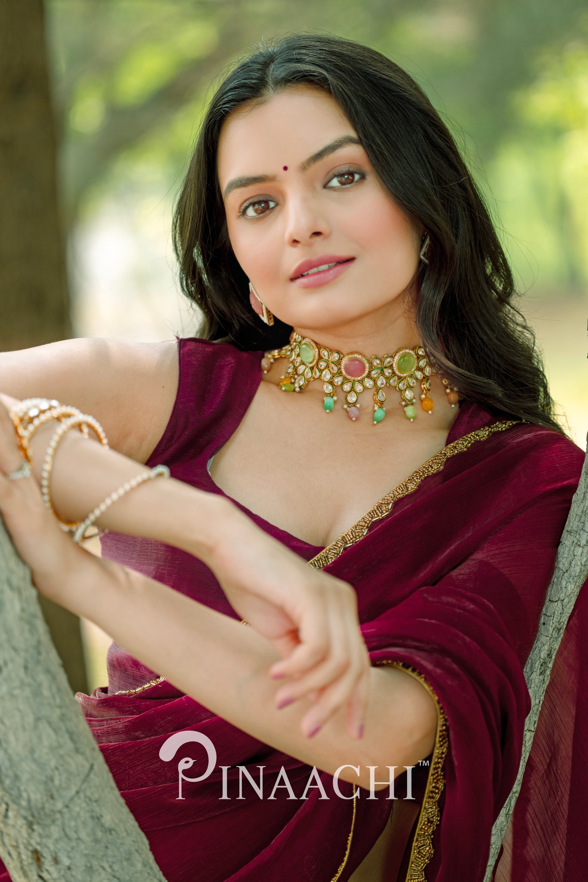 Woman wearing Pinaachi maroon chiffon saree with gold border and traditional jewelry outdoors