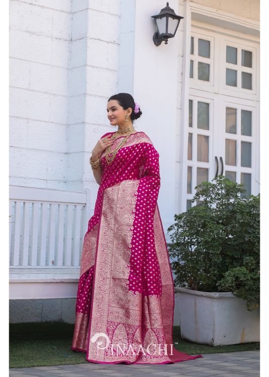 Woman wearing Pinaachi Pink Banarasi Silk Saree with intricate gold patterns standing outdoors near white building