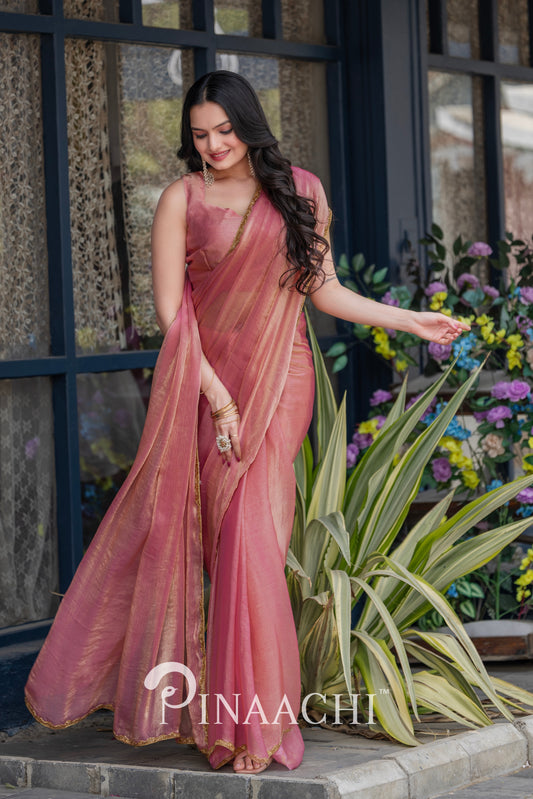 Elegant woman wearing pinaachi solid pink chiffon saree with golden border in a garden setting