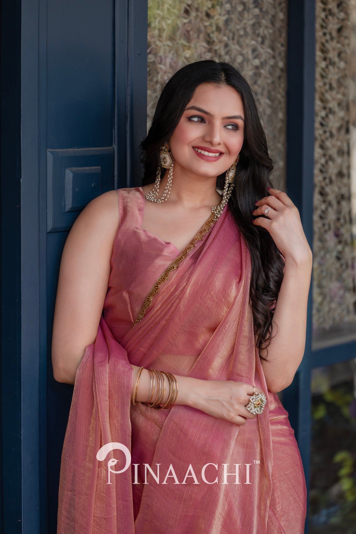 Elegant woman wearing a pinaachi solid pink chiffon saree with gold border and matching accessories