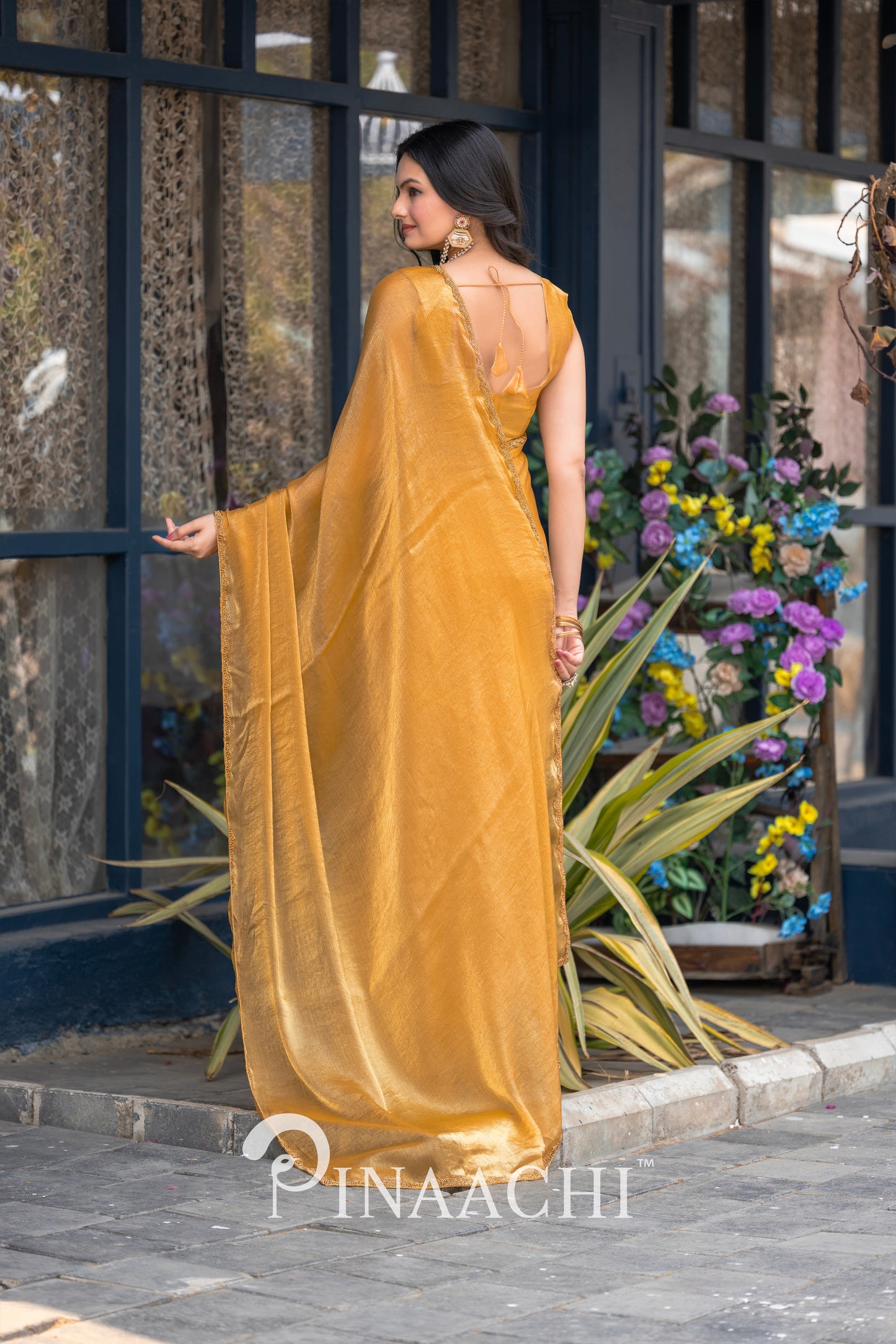 Pinaachi solid yellow chiffon saree draped elegantly on a model standing outdoors near plants and flowers