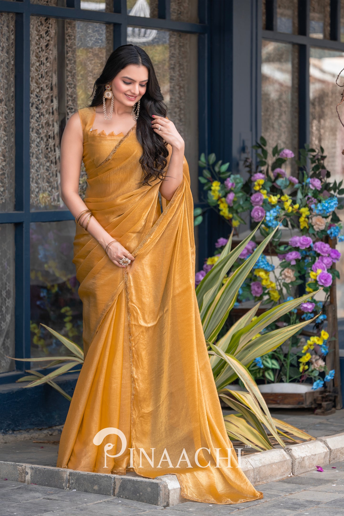 Woman wearing pinaachi solid yellow chiffon saree standing outdoors near plants and flowers