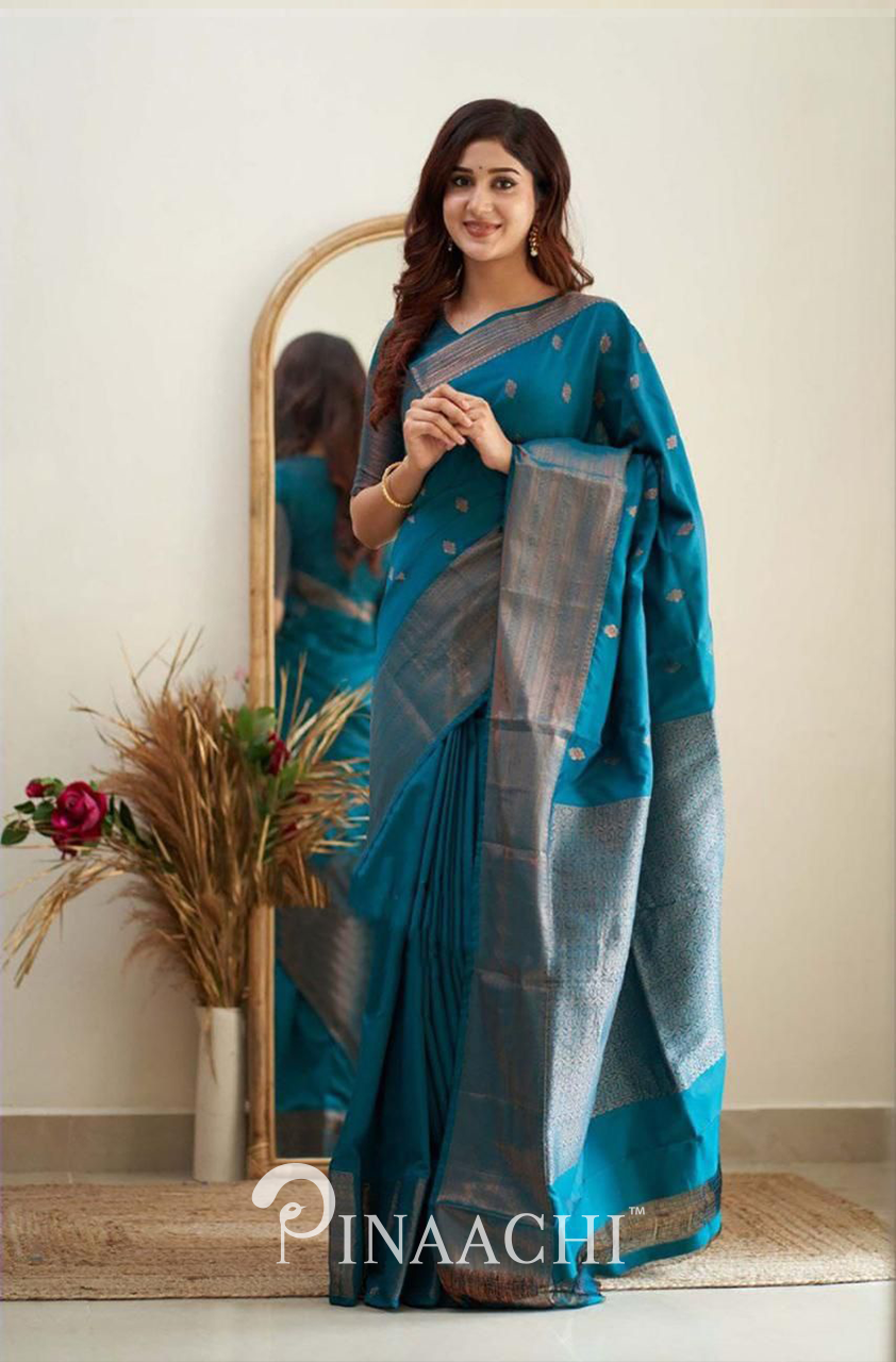 Woman wearing Pinaachi Turquoise Litchi Silk Saree standing in front of a mirror with floral decor