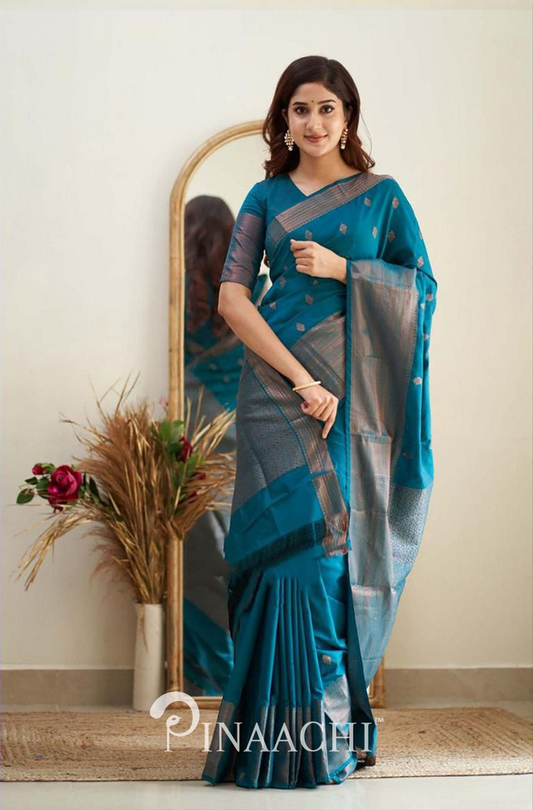 Woman wearing Pinaachi Turquoise Litchi Silk Saree posing indoors with mirror and decorative plants