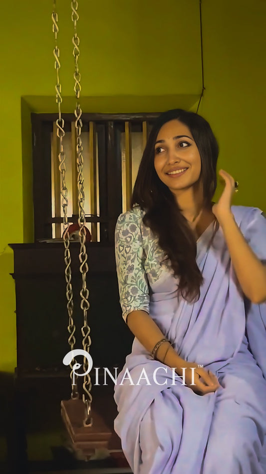 Woman wearing a lavender cotton handloom saree, smiling, sitting on a swing indoors