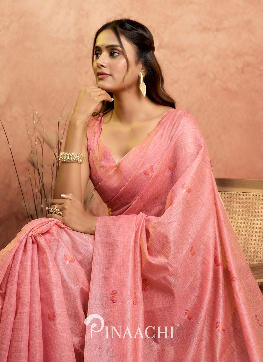 Pinaachi pink jamdani saree with delicate floral embroidery worn by woman seated on chair