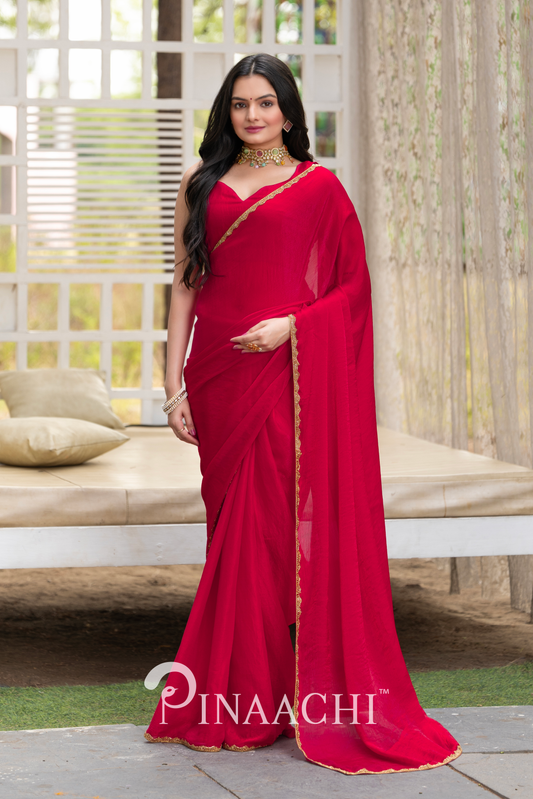 Pinaachi solid cherry red chiffon saree worn by model with gold border in elegant indoor setting