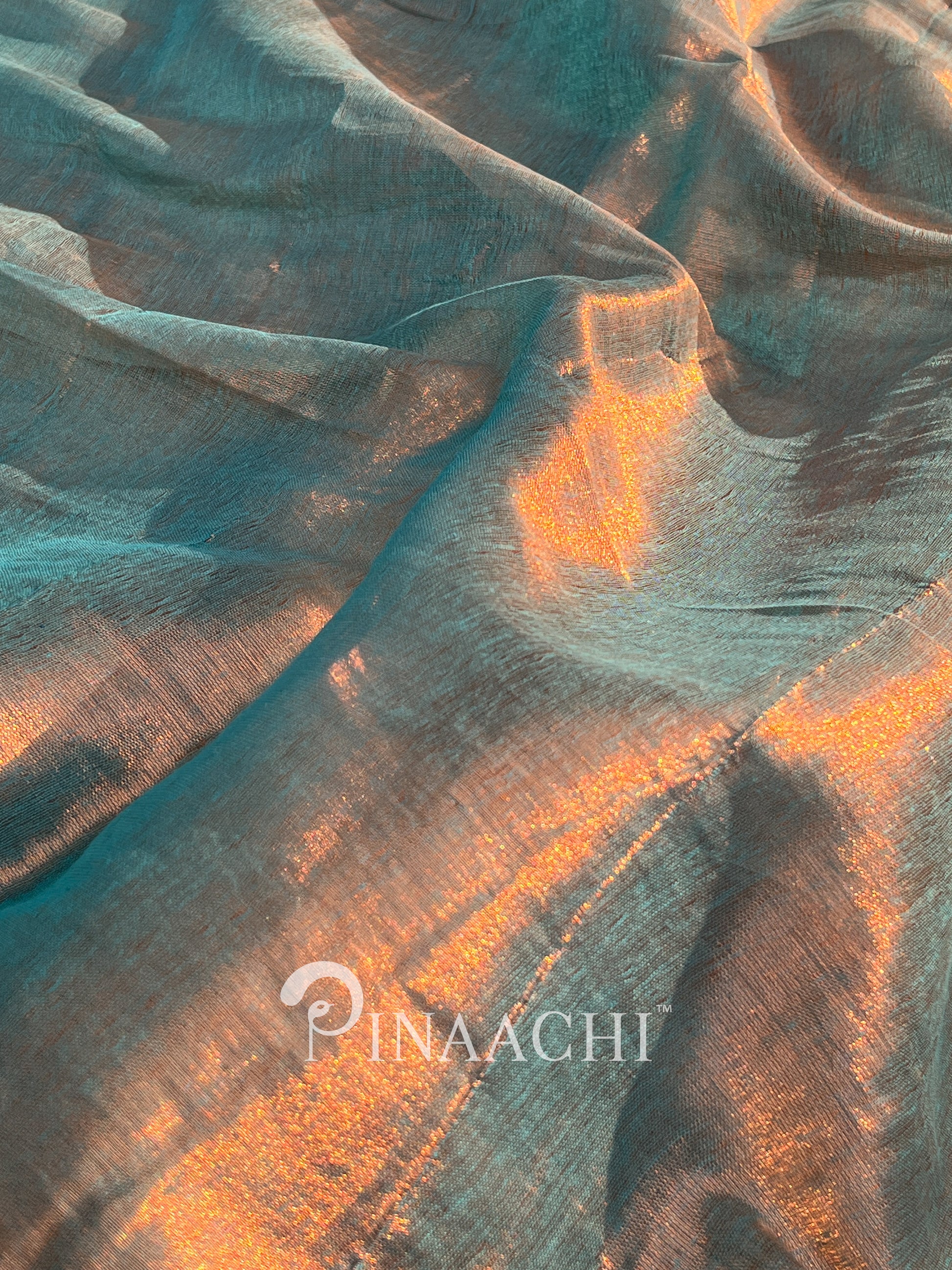 Close-up of textured fabric with orange and blue patterns, featuring the brand 'Pinaachi'.