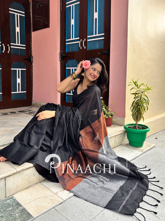 Elegant black cotton saree with zari border styled elegantly on a woman in a picturesque setting