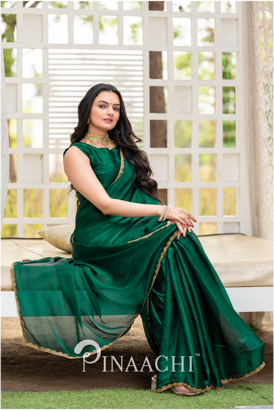 Woman wearing a Pinaachi bottle green chiffon saree with gold border sitting gracefully indoors