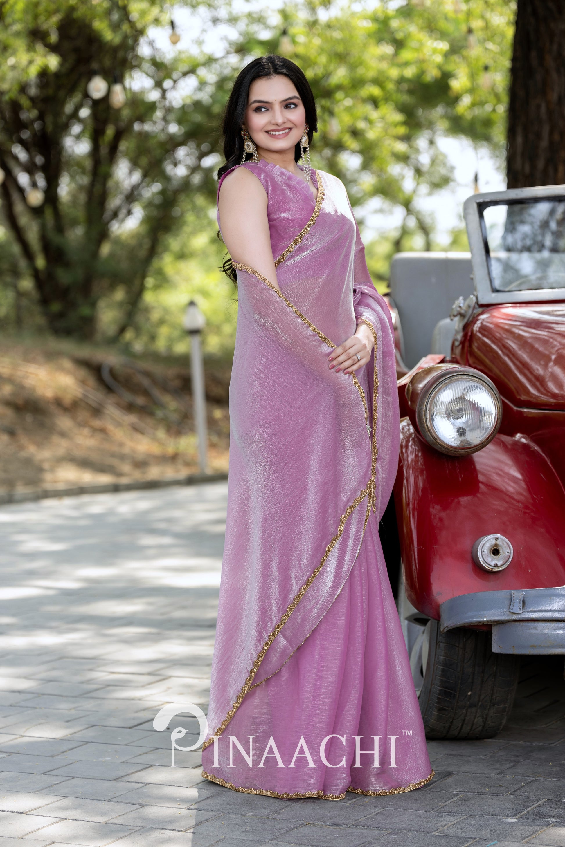 Woman wearing Pinaachi lavender chiffon saree with gold border standing beside a vintage red car outdoors