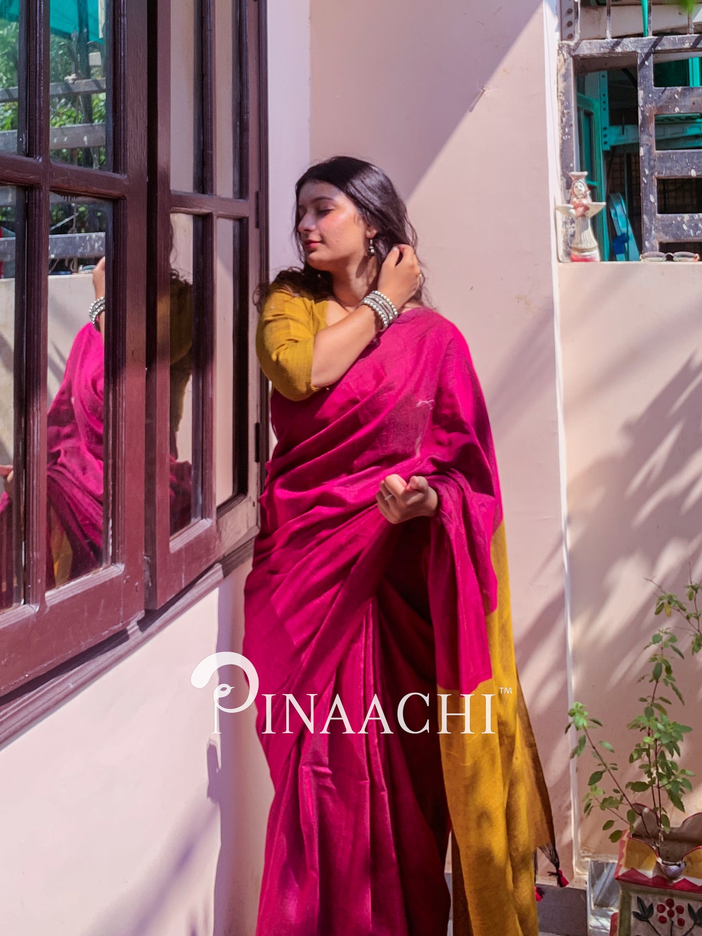 Model wearing a magenta pink cotton handloom saree with a contrasting yellow blouse in a sunlit room