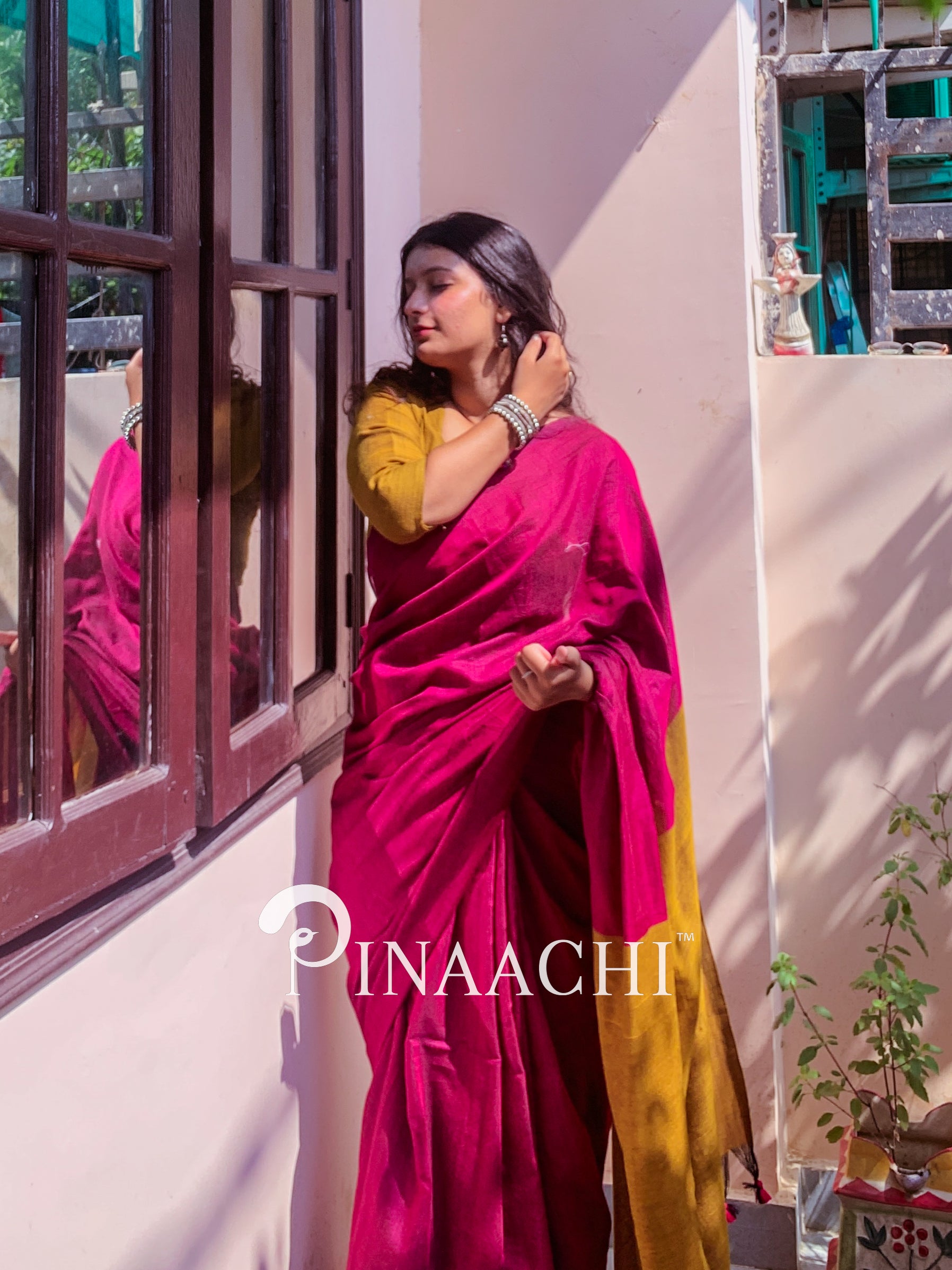 Model wearing a magenta pink cotton handloom saree with a contrasting yellow blouse in a sunlit room