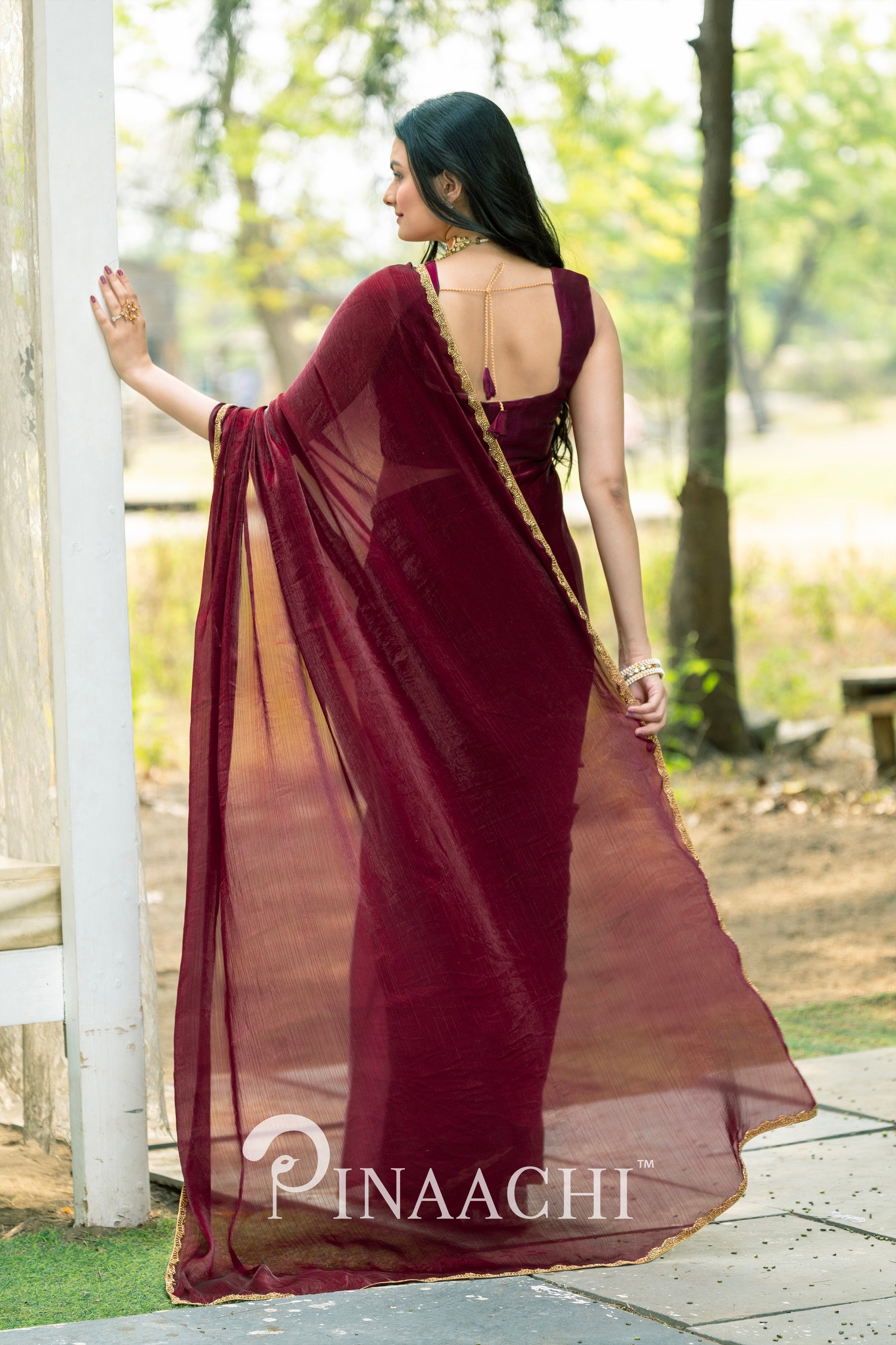 Woman wearing Pinaachi maroon chiffon saree with sleeveless blouse standing outdoors