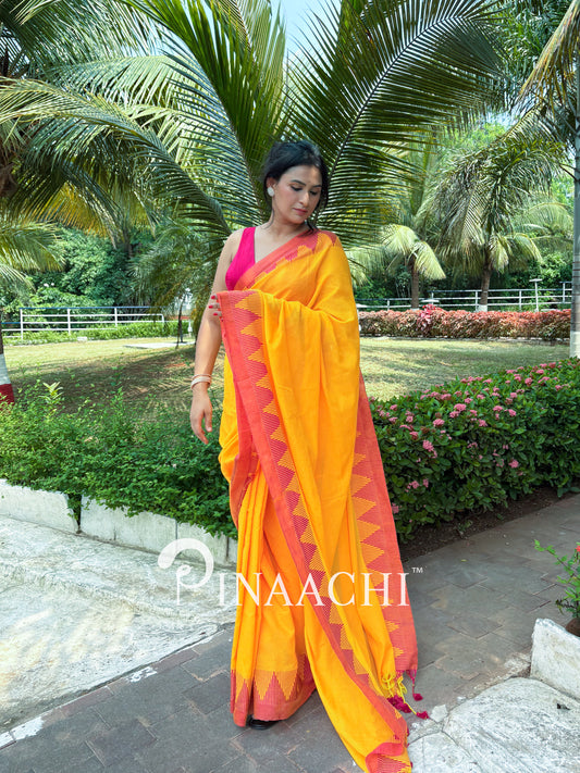 Woman wearing a mustard yellow cotton saree with contrasting borders in a lush garden setting