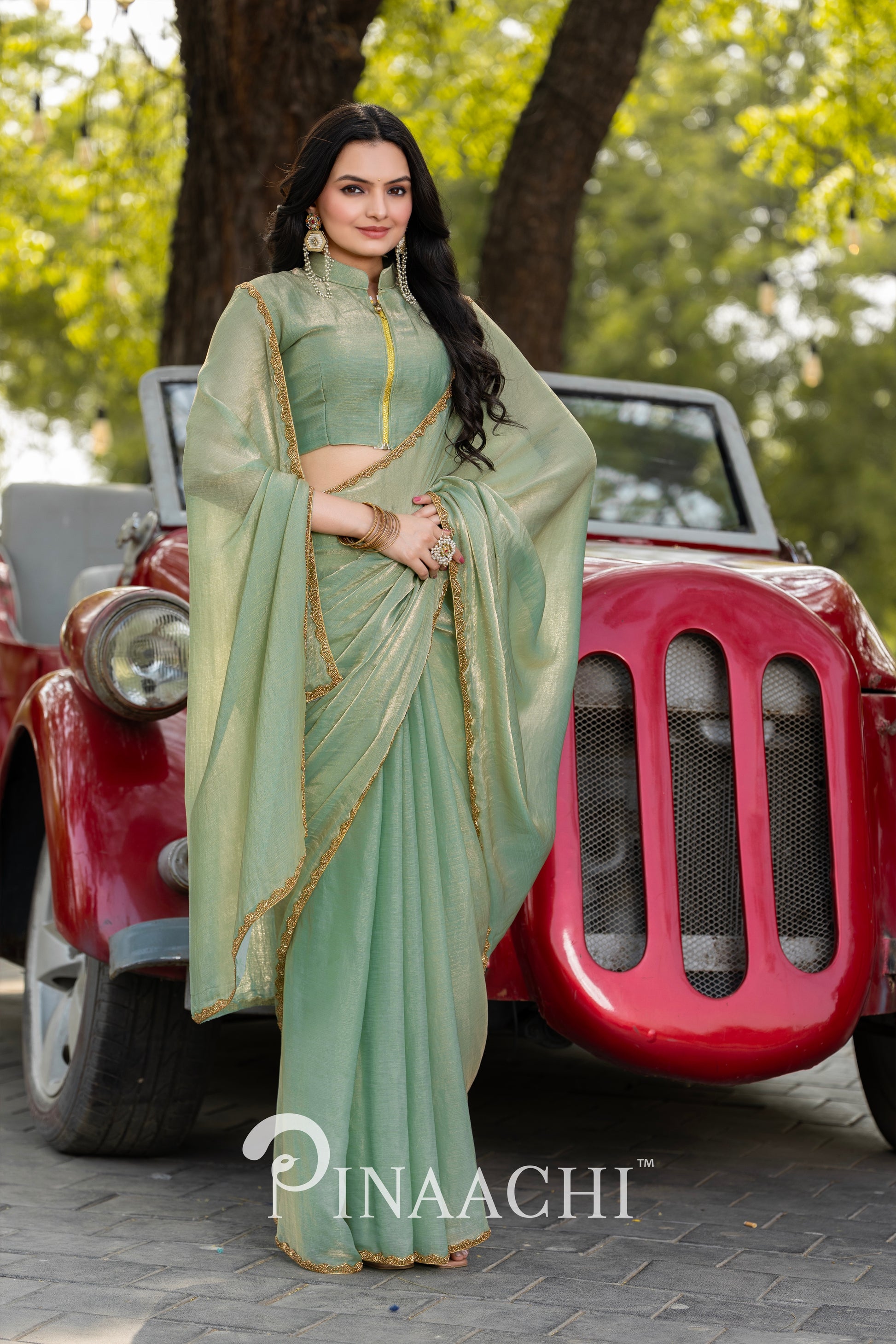Woman wearing pinaachi pista green chiffon saree with golden border standing in front of a vintage red car