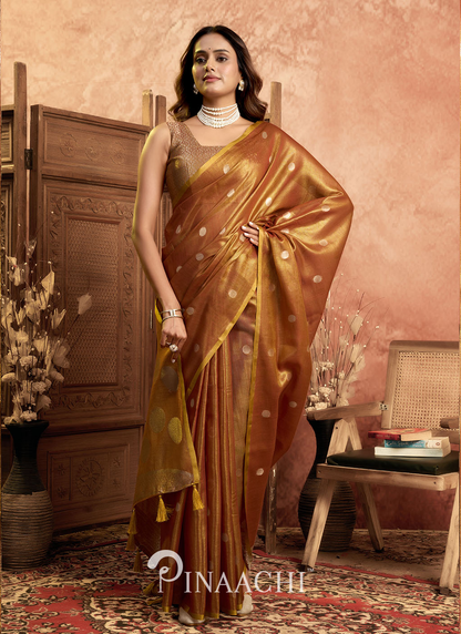 Woman wearing a golden brown Pinaachi polka tissue silk saree with traditional jewelry in an elegant room