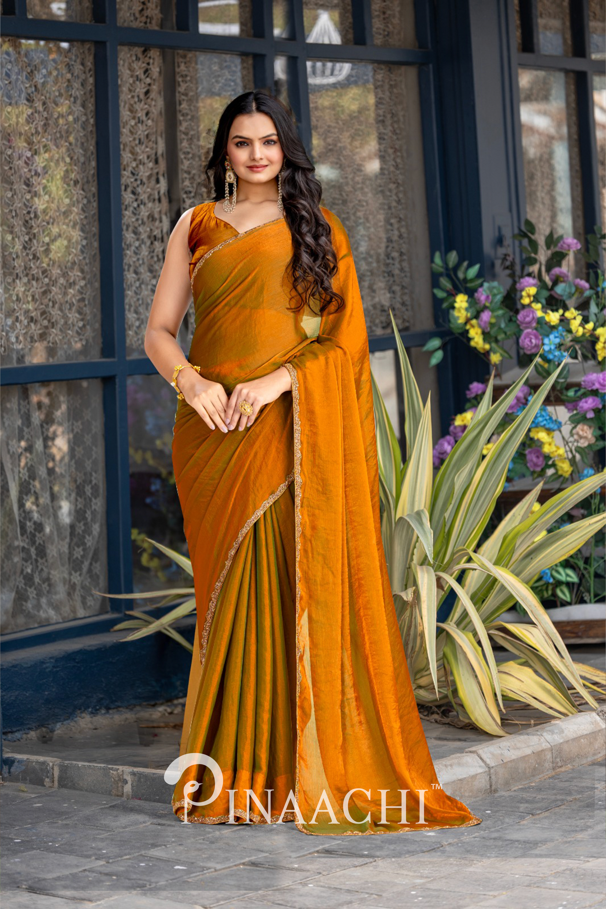 Pinaachi solid gold chiffon saree worn by a woman with long hair standing outdoors near plants