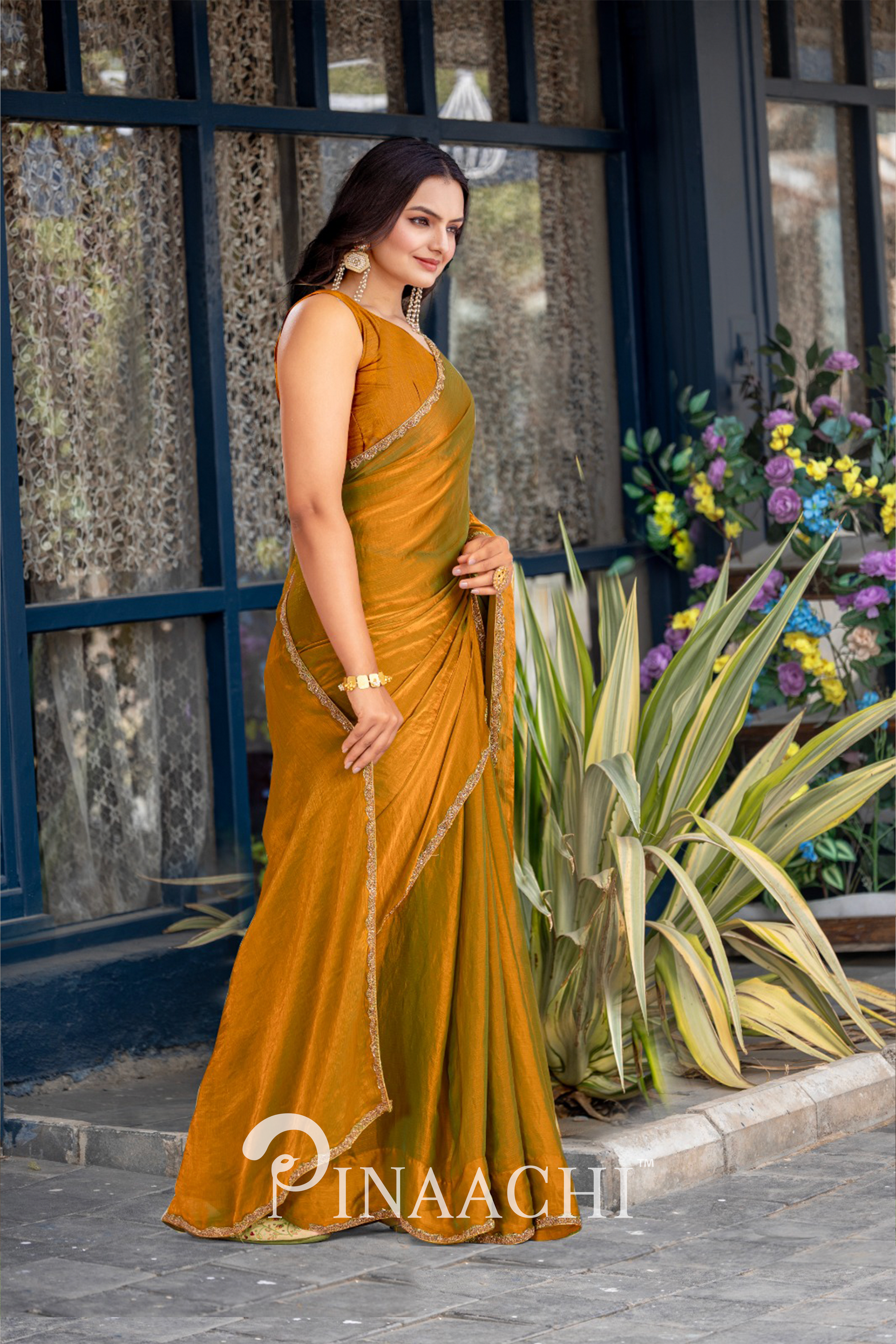 Elegant woman wearing pinaachi solid gold chiffon saree standing outdoors near plants