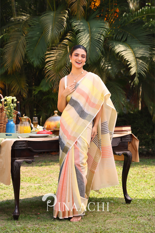 Woman wearing Pinaachi striped linen silk saree in pastel colors standing outdoors near a table