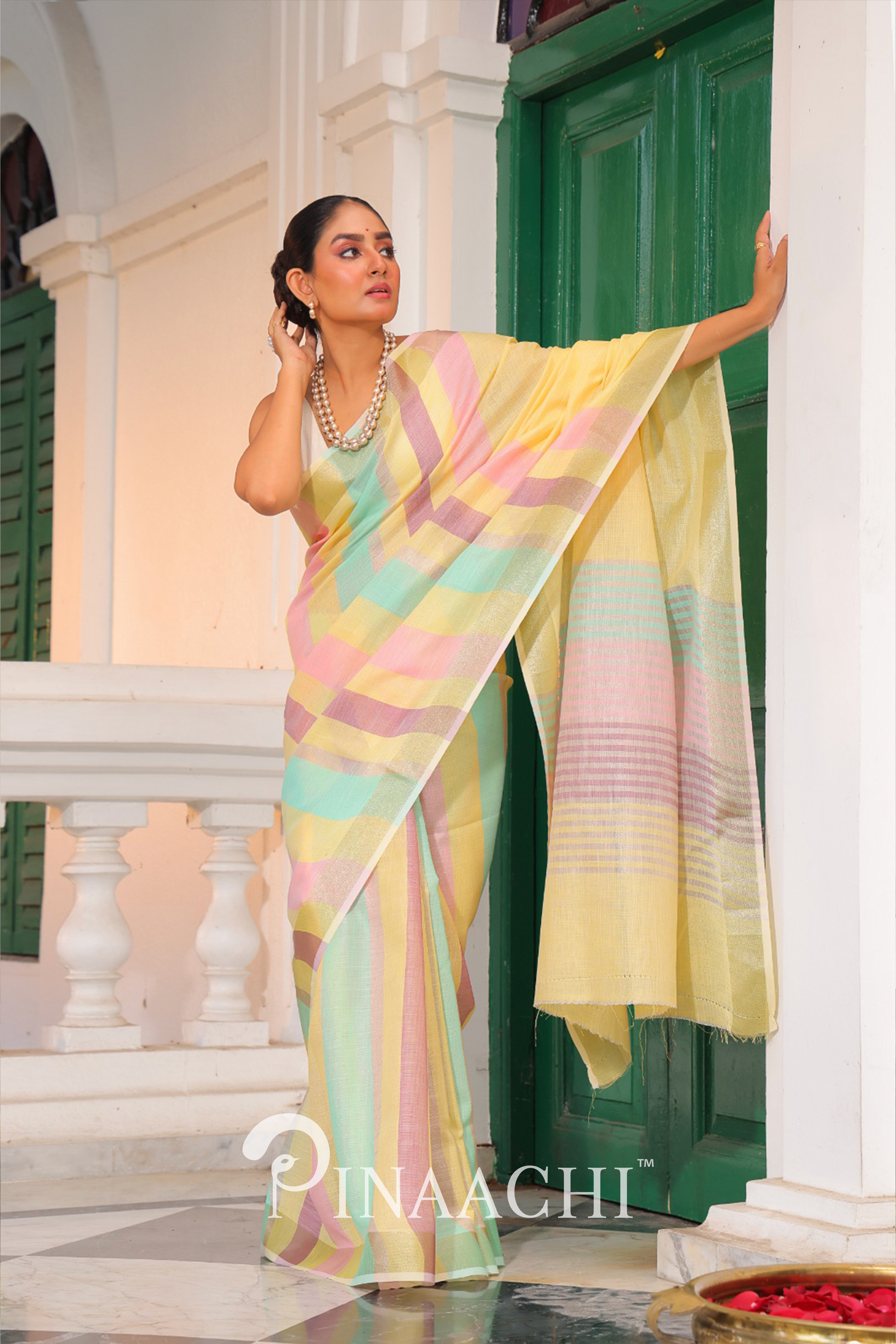 Woman wearing Pinaachi Summer Stripe Linen Silk Saree with pastel yellow and multicolor stripes standing by green door