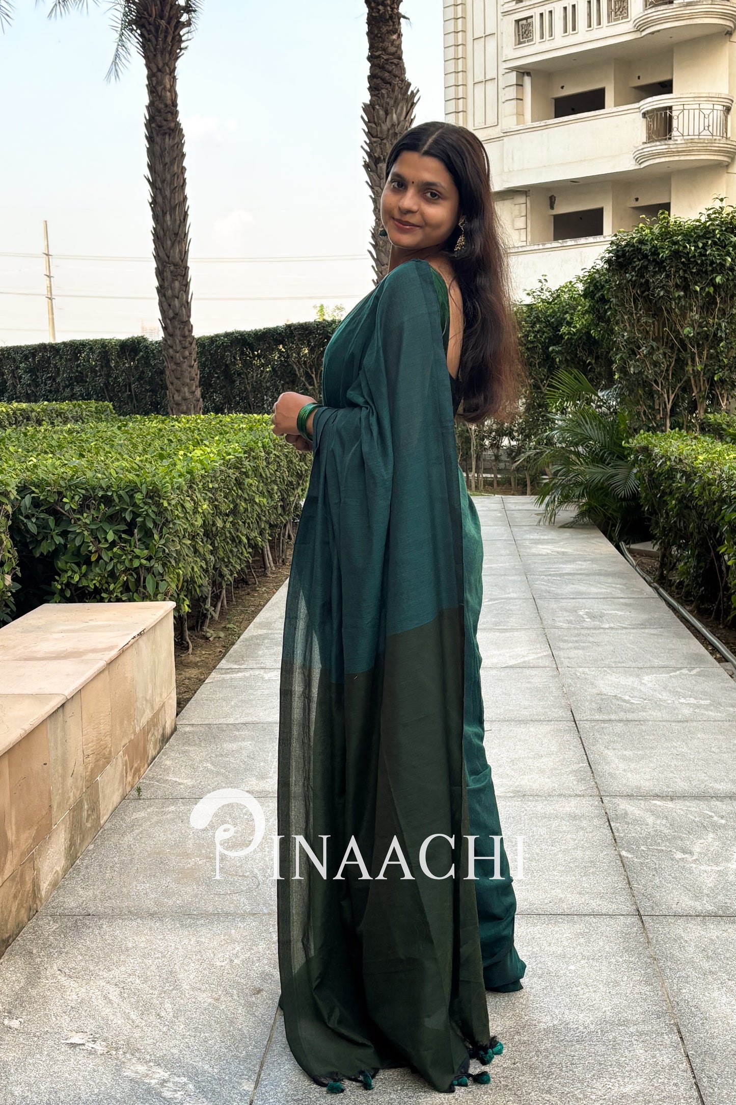 Elegant woman wearing a teal green cotton saree, styled with a beautiful drape outdoors