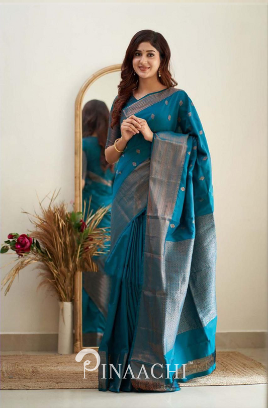 Woman wearing Pinaachi Turquoise Litchi Silk Saree standing in front of a mirror with floral decor